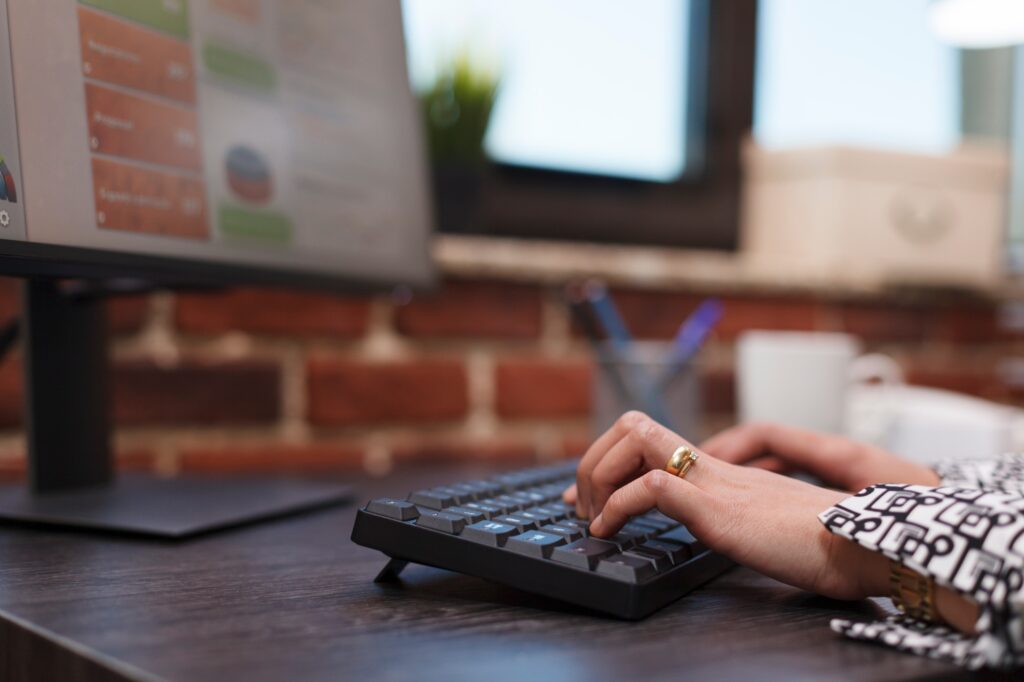 Close up of advertising agency employee hands typing on keyboard and working on research charts